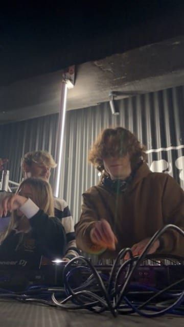 A DJ in headphones working the decks, phone light on the mixer.
