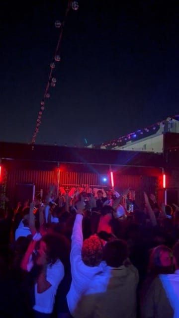 A crowd dancing under red lights and string lights.