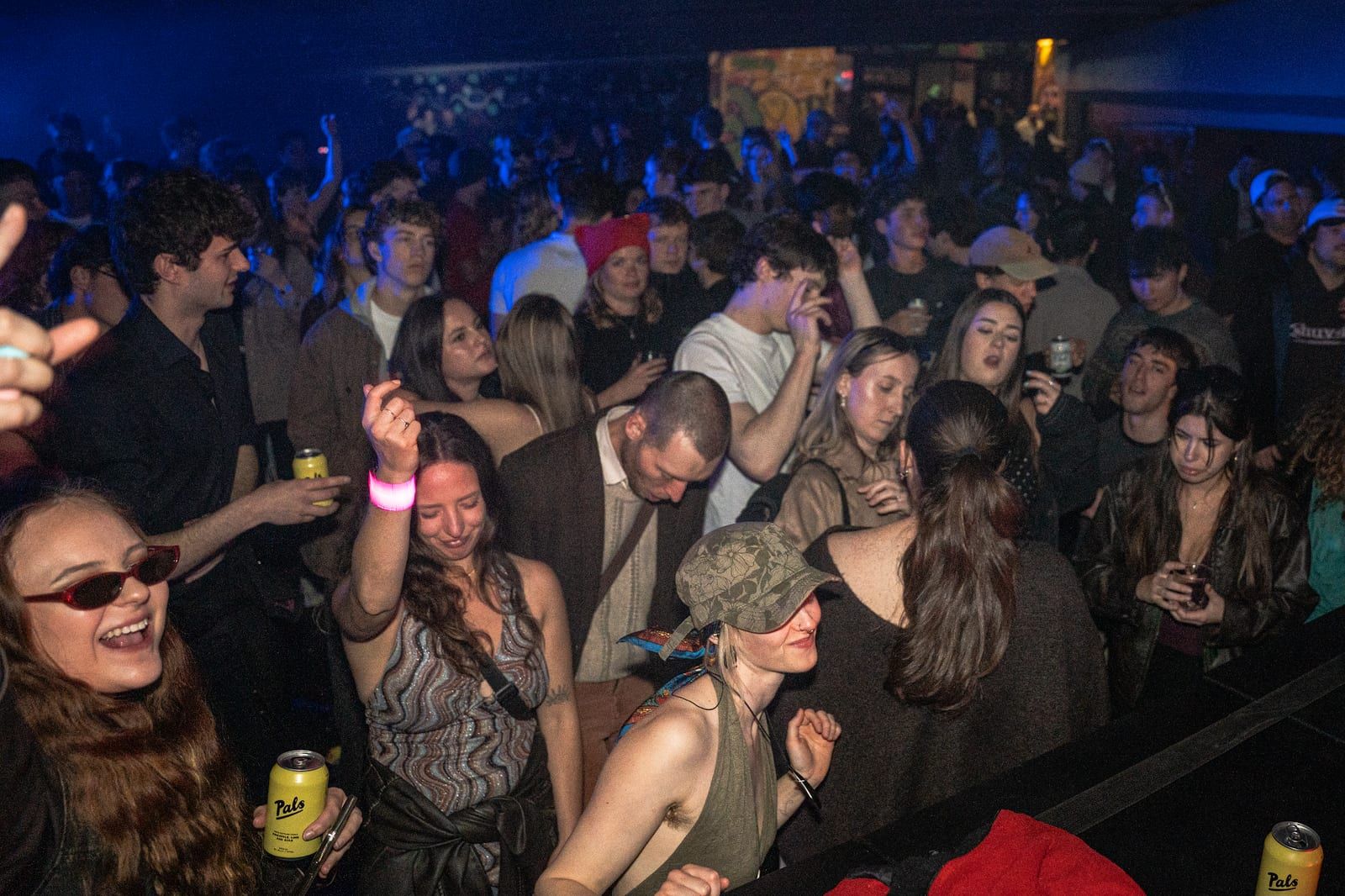 Front of the crowd laughing and dancing, one in tiny sunglasses holding a can.