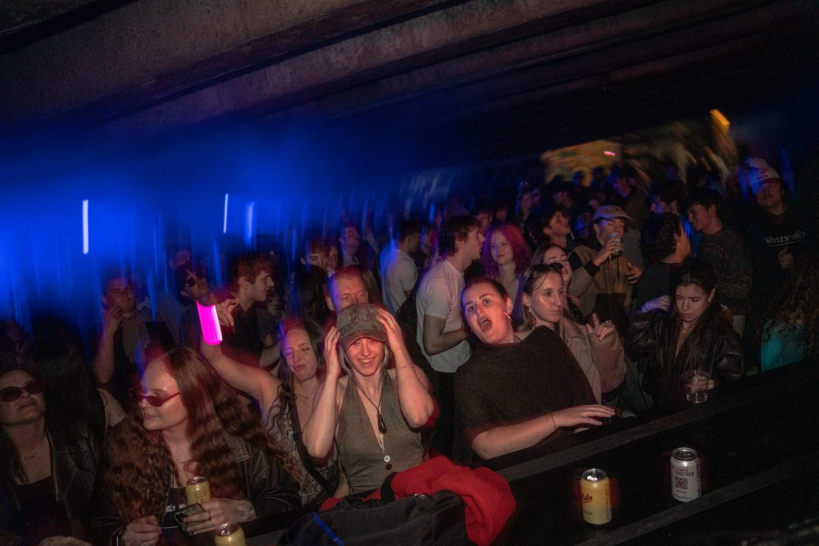 Packed crowd under deep blue light, hands up.