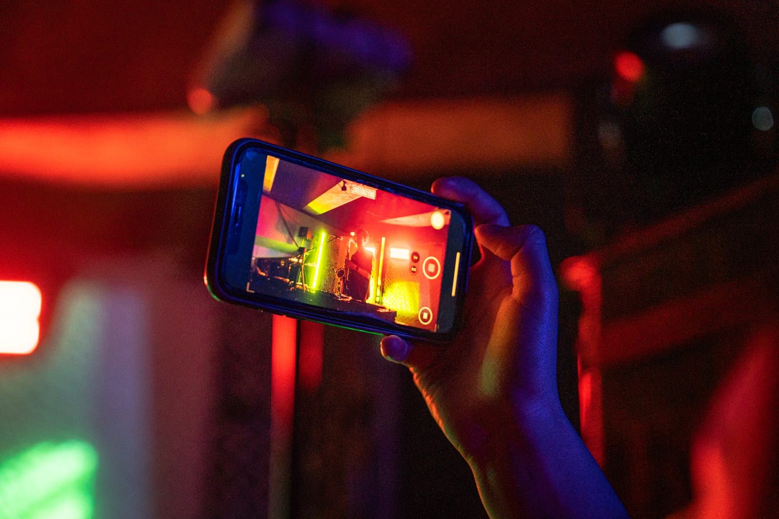 A phone held up in red light, filming the stage.