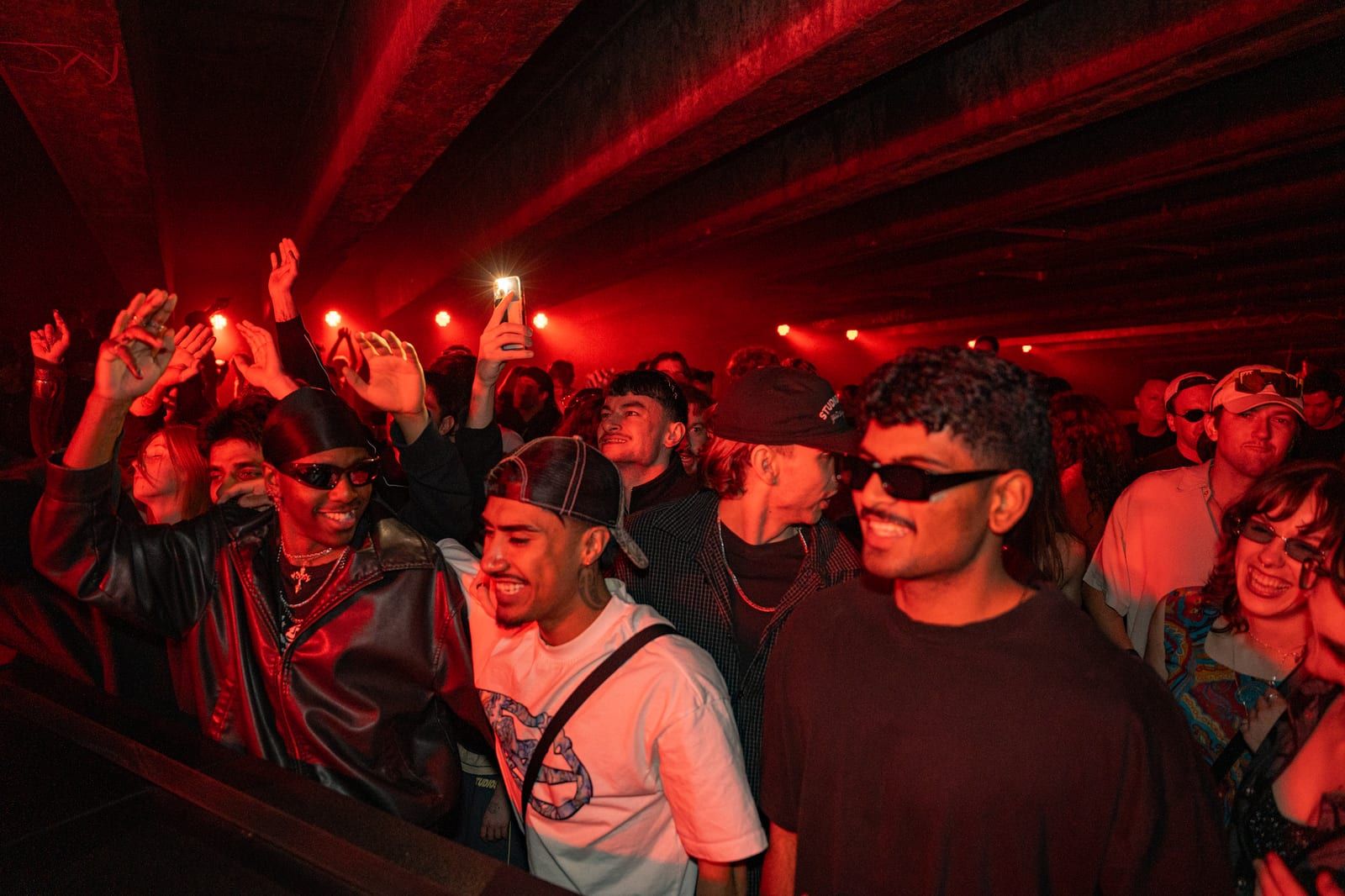 Front row in red light, arms out, one holding up a lighter.