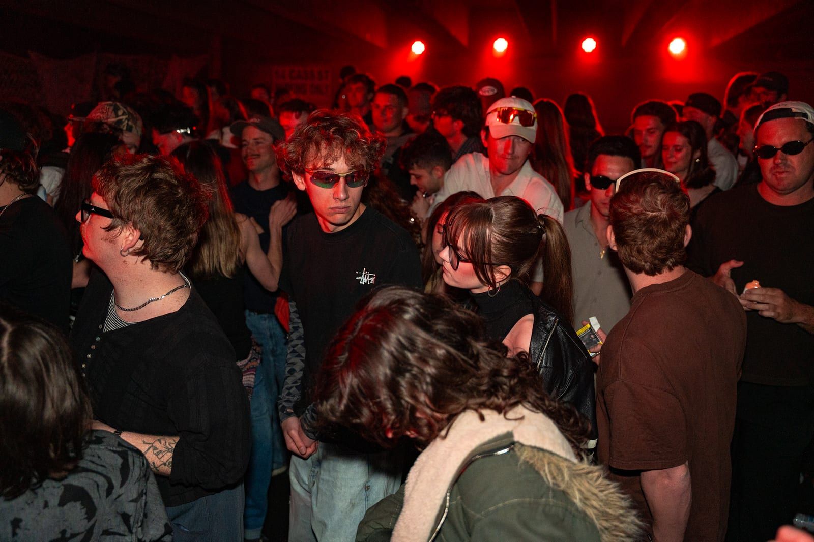 Crowd in sunglasses dancing in red light.