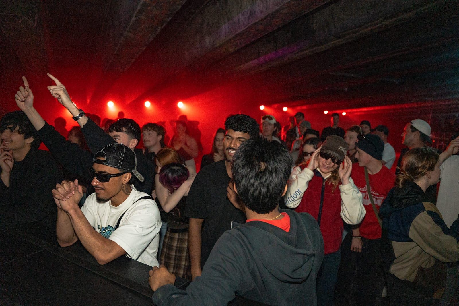 A crowd with hands up in red light and haze.